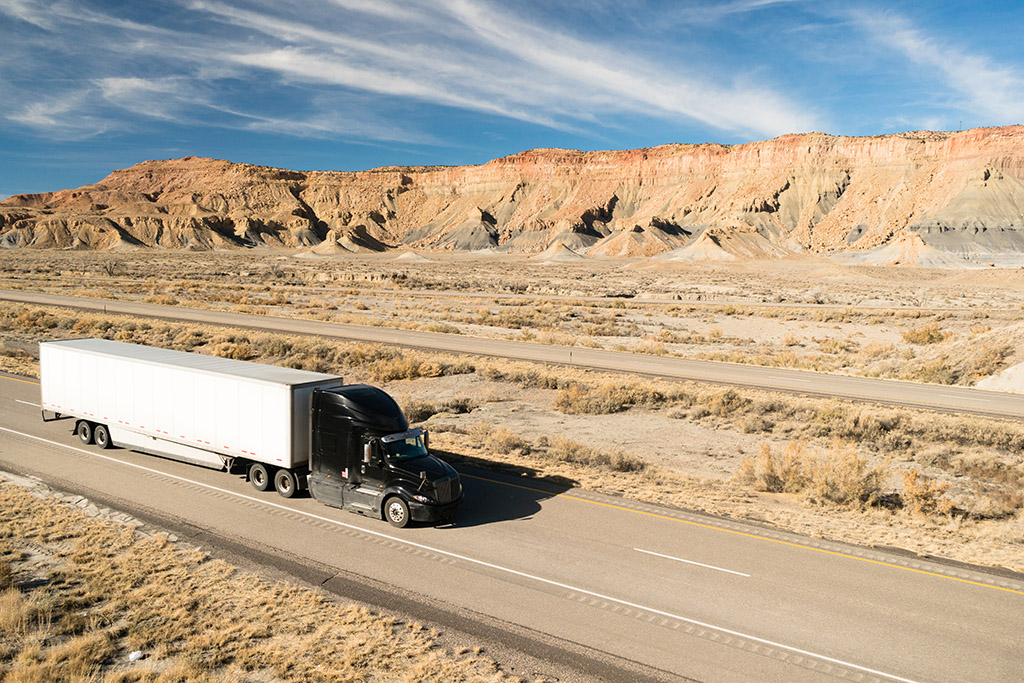 A black full truckload big rig rolls across Utah on a highway