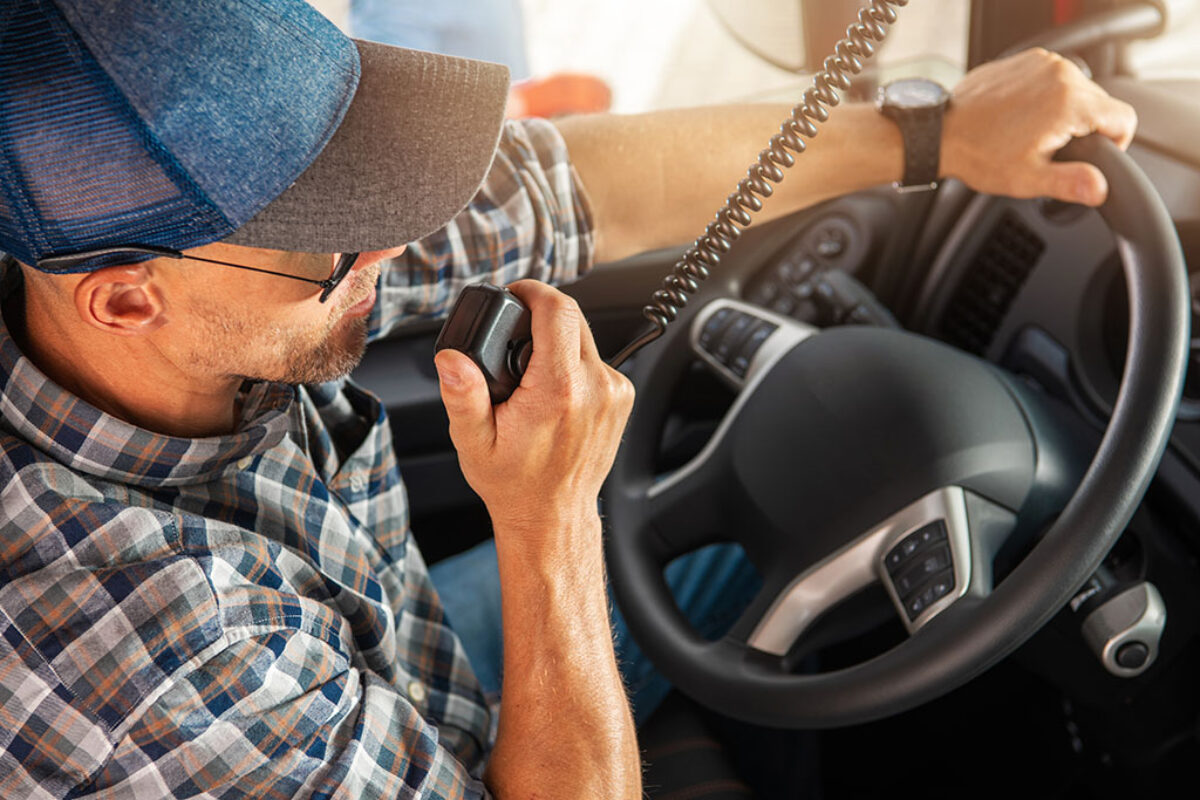 Caucasian Trucker in His 40s Making Conversation Using CB Radio Inside His Semi Truck Cabin. Convoy Truck Drivers Communication Theme.